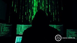 Hacker cu glugă în fața unor monitoare cu cod verde în stil Matrix